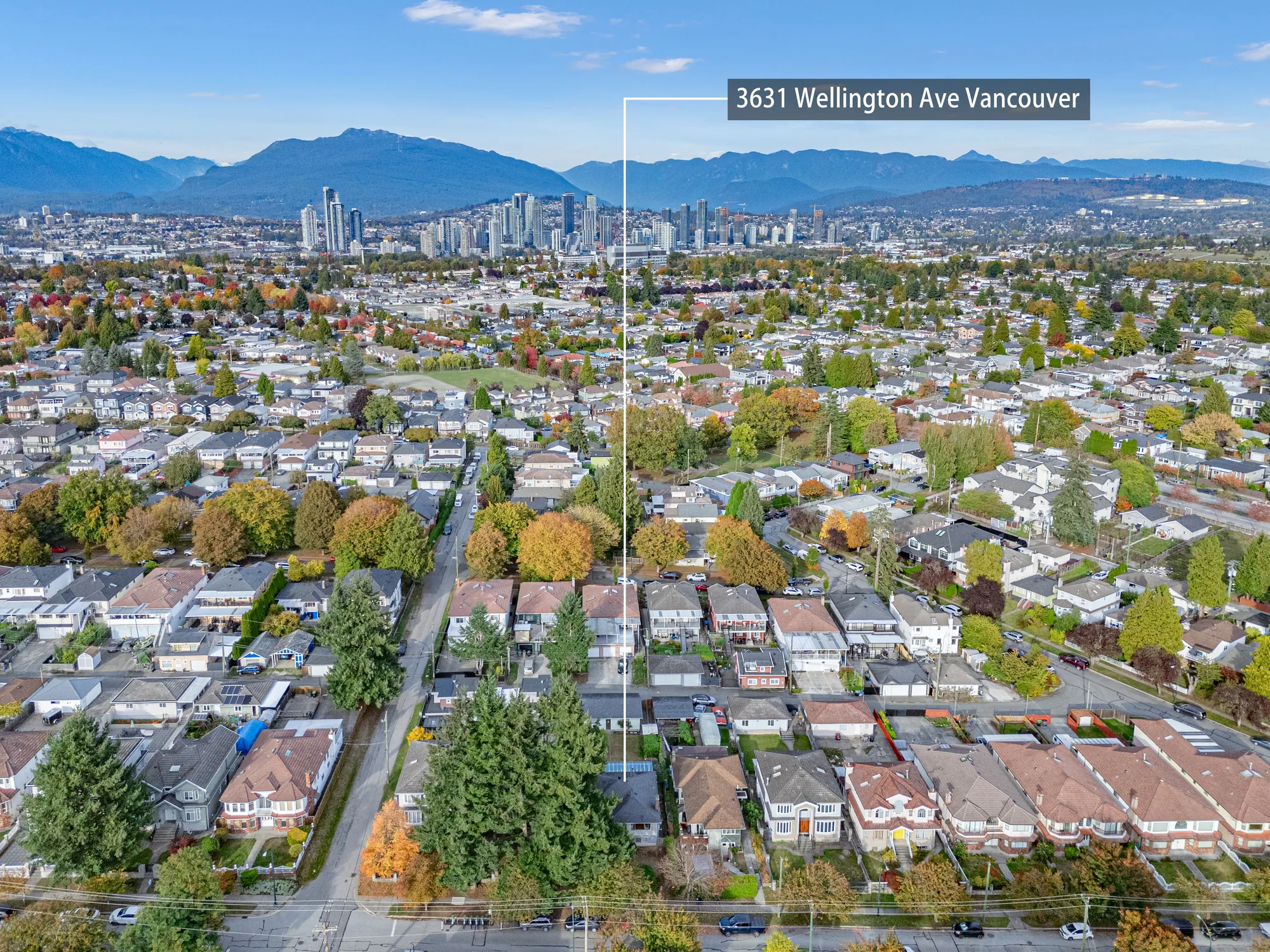 A high view north over the neighbourhood to the North Shore mountains and the downtown towers, the house marked with a label reading 3631 Wellington Ave Vancouver