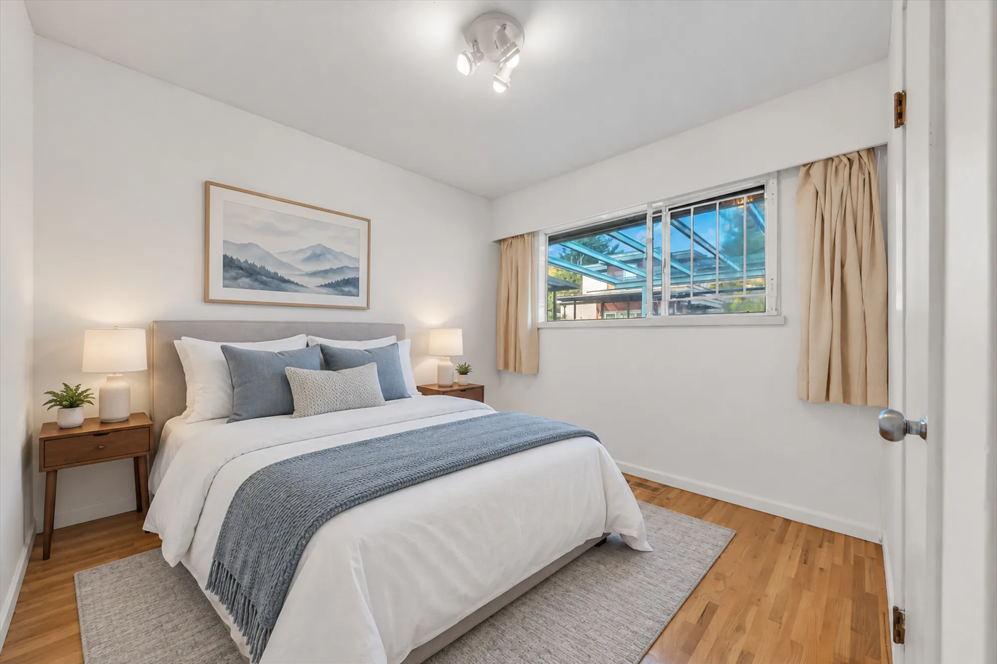 The same frame virtually staged: a bed with a blue throw, night tables and lamps, a rug, a mountain print