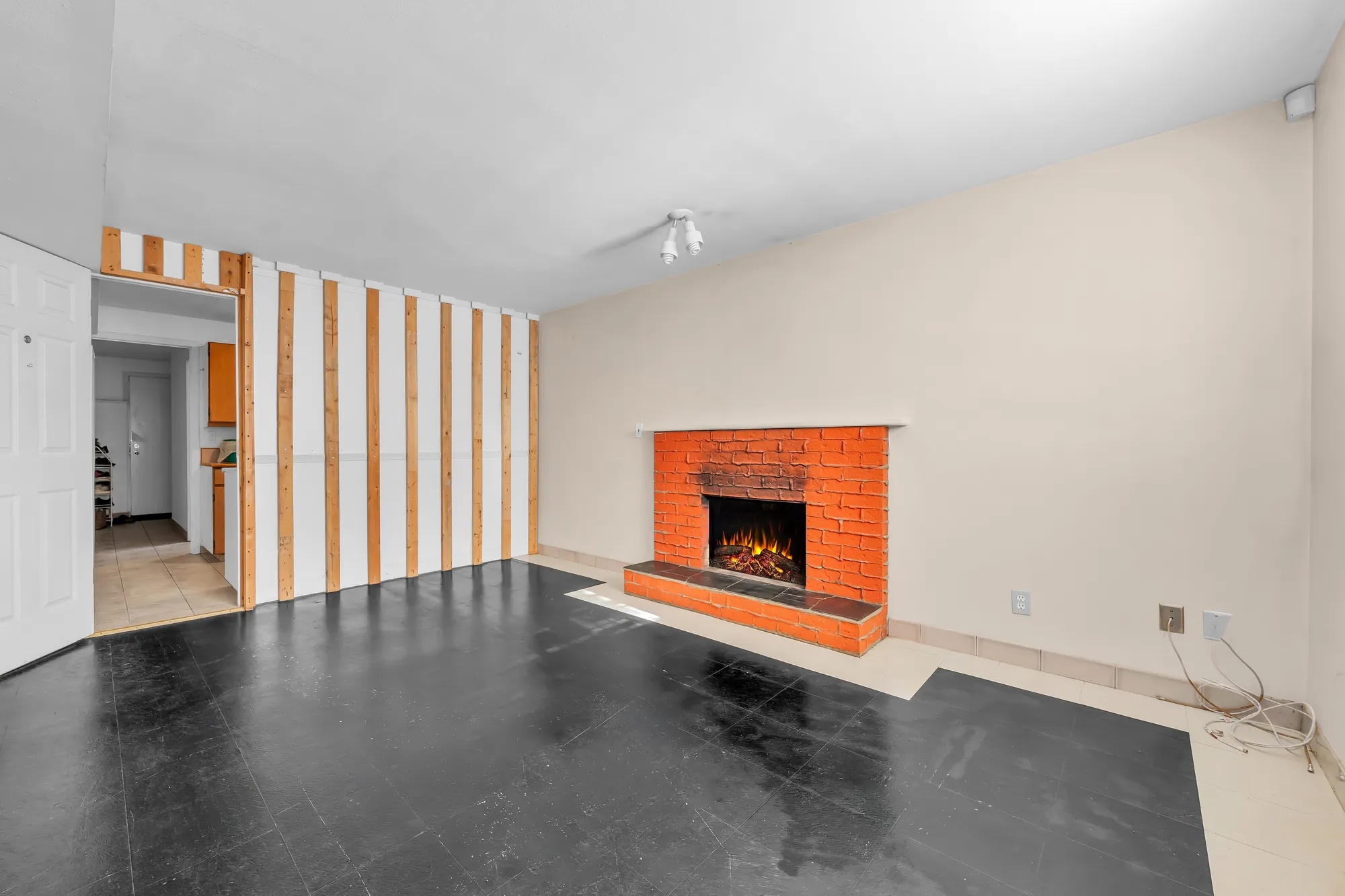 The family room toward the doorway: an open door to the hall, a wall of wood slats, the brick fireplace