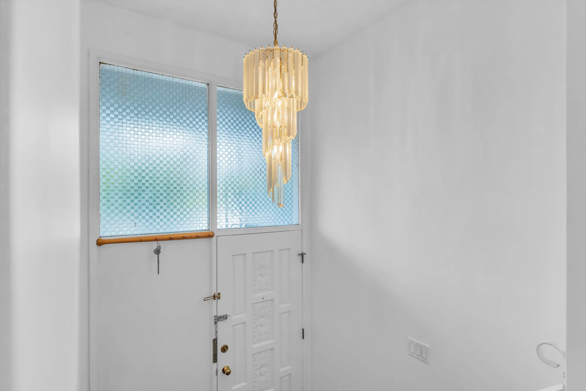 The front door from inside: a white door under a panel of frosted glass, a crystal chandelier