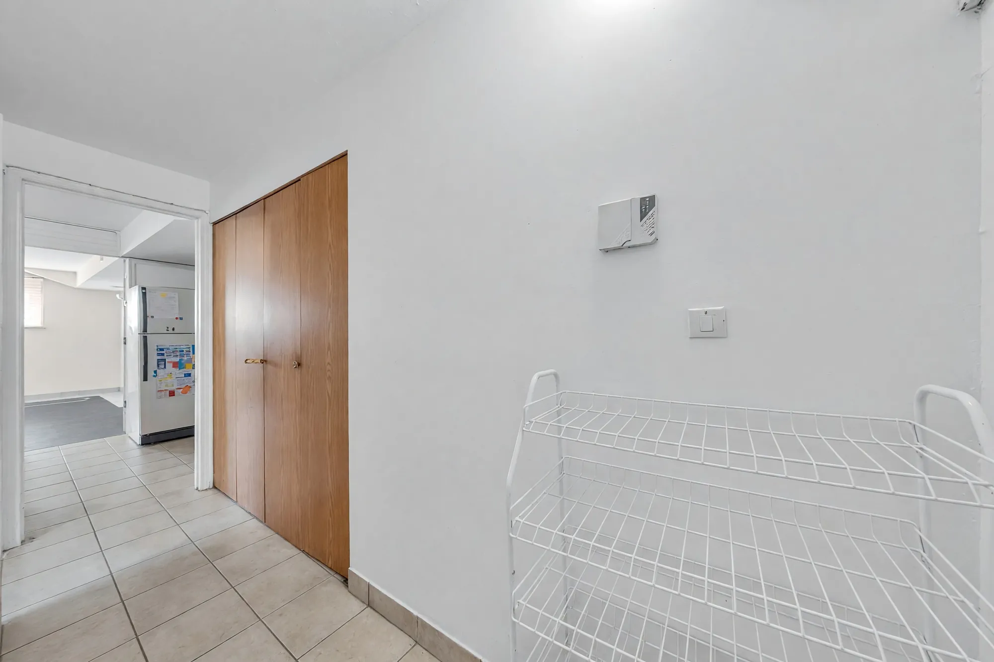 The lower hall: a tile floor, wood closet doors, an empty wire shoe rack, a bedroom beyond