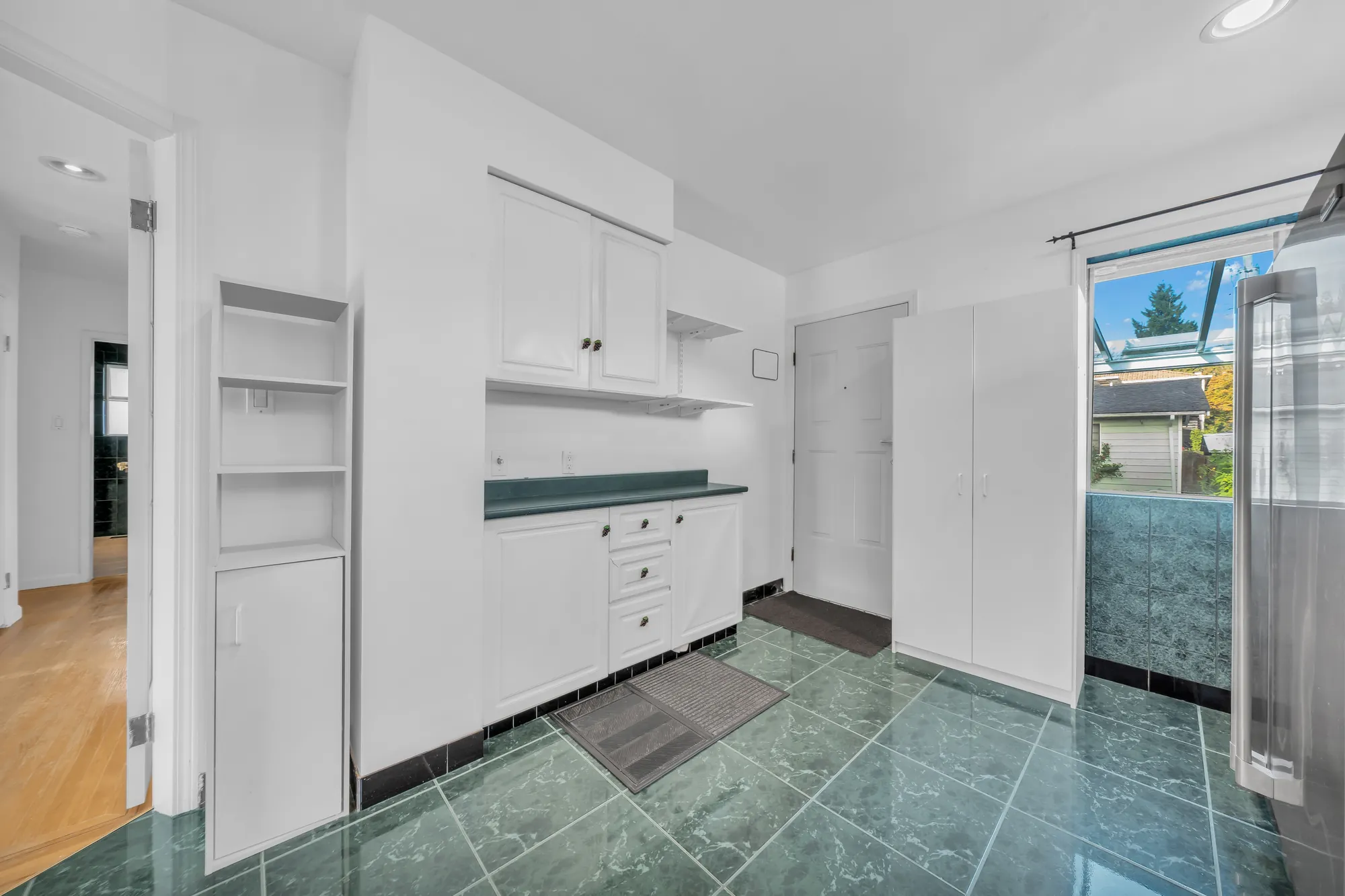 The kitchen toward the back door: open shelving built into the wall, white cabinets and drawers, the doorway to the hall at the left