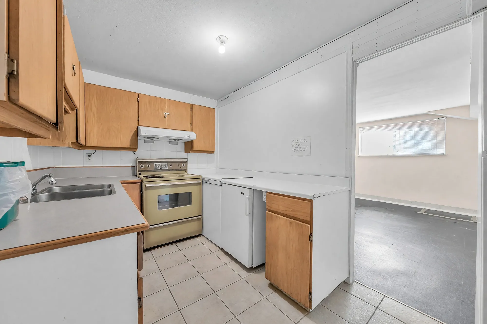 The lower kitchen: wood cabinets, a range, a sink, white counters, the family room through the doorway