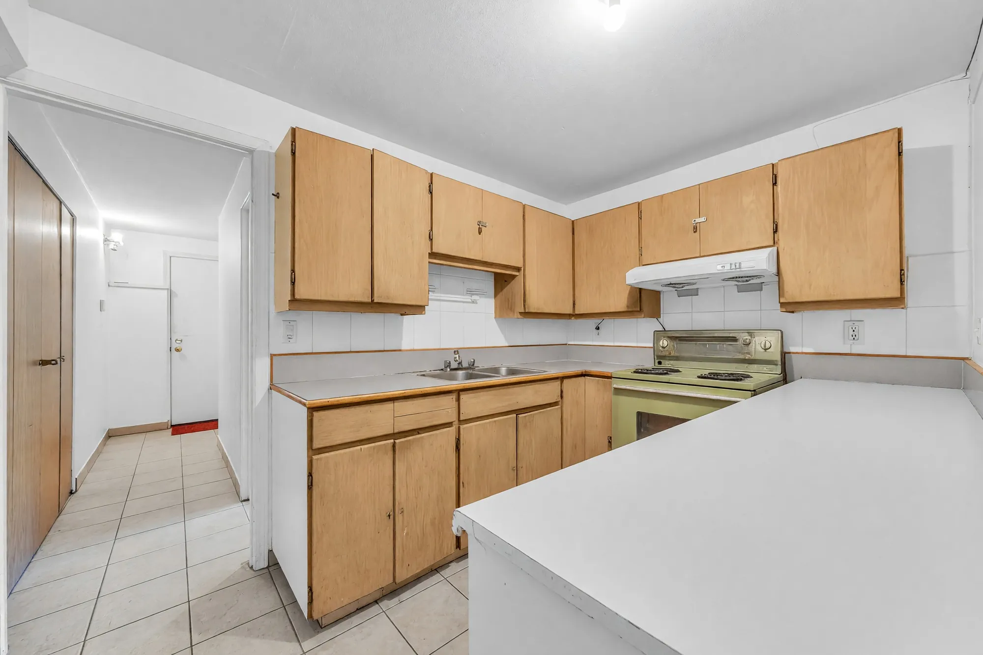 The lower kitchen toward the hall: wood cabinets, a peninsula counter, a tiled floor