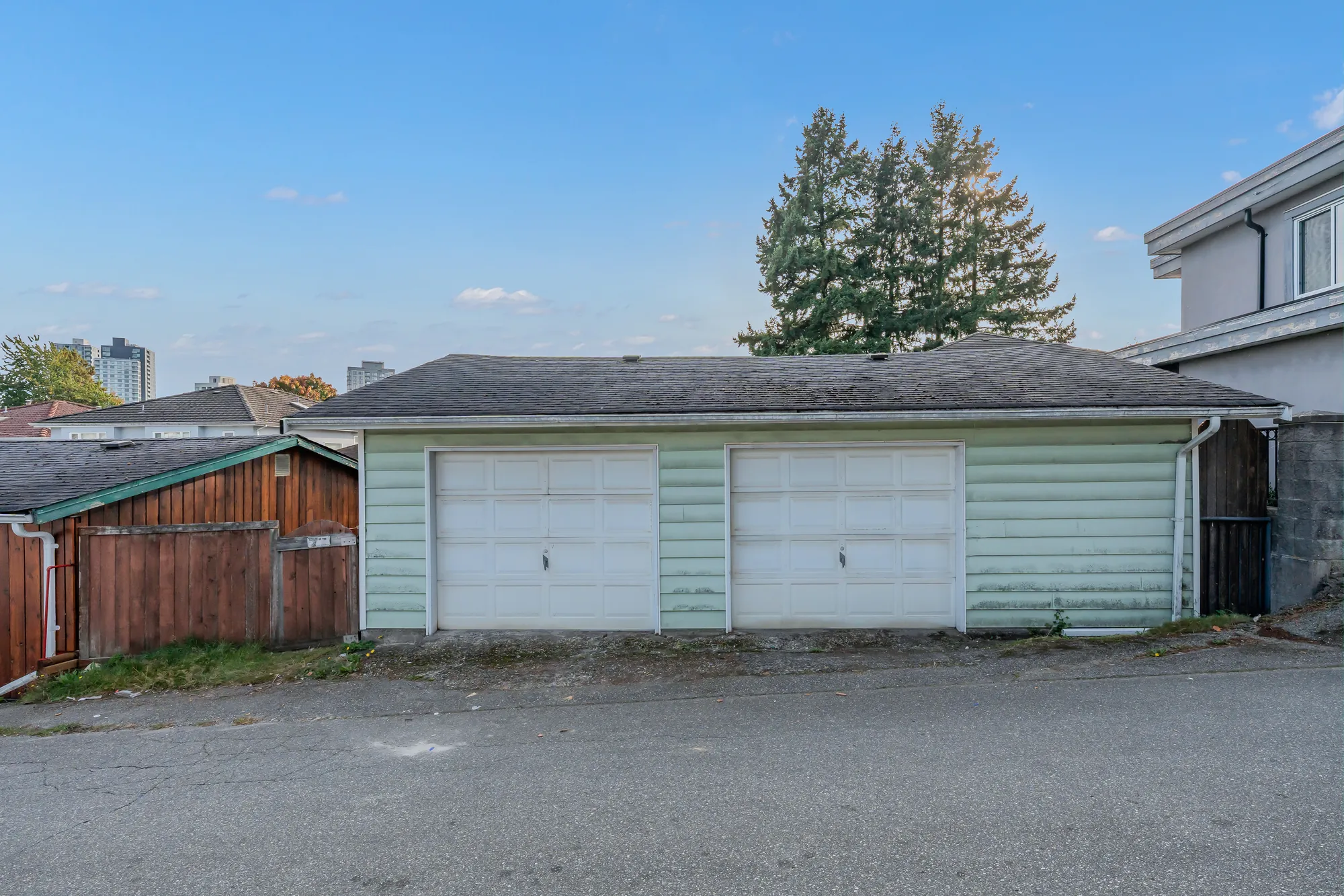 The garage from the lane: two white overhead doors in pale green siding, a paved lane